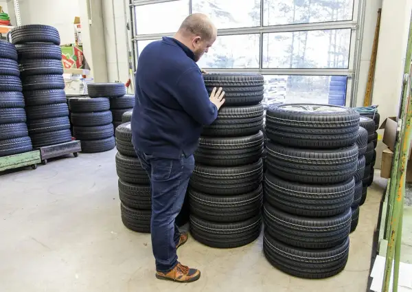 Mężczyzna wybiera najlepsze opony spośród wielu stosów. W magazynie panuje porządek, a opony są ułożone w równych rzędach.
