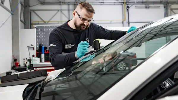 Mechanik w okularach ochronnych i rękawiczkach naprawia szybę samochodową.