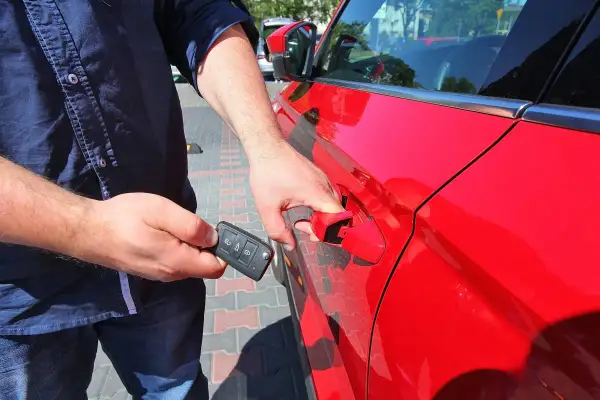 Mężczyzna z kluczykiem w dłoni otwiera czerwony samochód, korzystając z systemu keyless go.