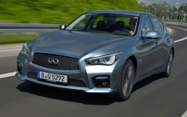 Srebrny infiniti samochód pędzi po autostradzie, kierowca w okularach przeciwsłonecznych cieszy się jazdą.