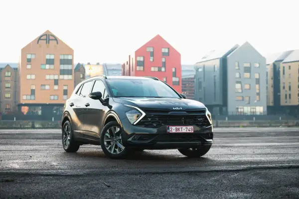 Czarny, mały SUV Kia Sportage stoi na mokrym asfalcie przed nowoczesnymi budynkami.