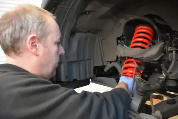 Mechanik w niebieskiej rękawiczce pracuje nad nowym, czerwonym, wylany amortyzator.